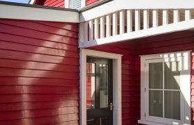 Red weatherboard entry with black front door, white trim and patterned tile threshold in afternoon sun.