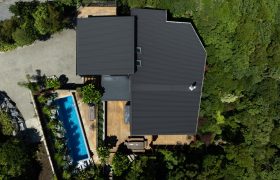 Aerial view of the roof and timber decks, with the pool and outdoor rooms set into dense bush.