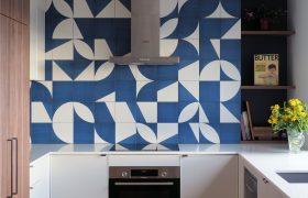 Kitchen with blue and white geometric tiled splashback, walnut cabinetry and white benchtops